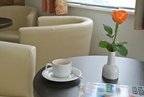 A round table with a white cup of coffee, a white vase with an orange rose, and a magazine. - Pension Paradiesgartl (Amstetten)