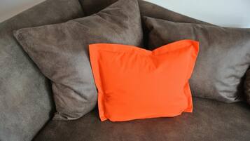 A brown sofa with a single orange pillow.