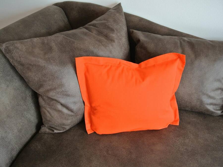 A brown sofa with a single orange pillow.
