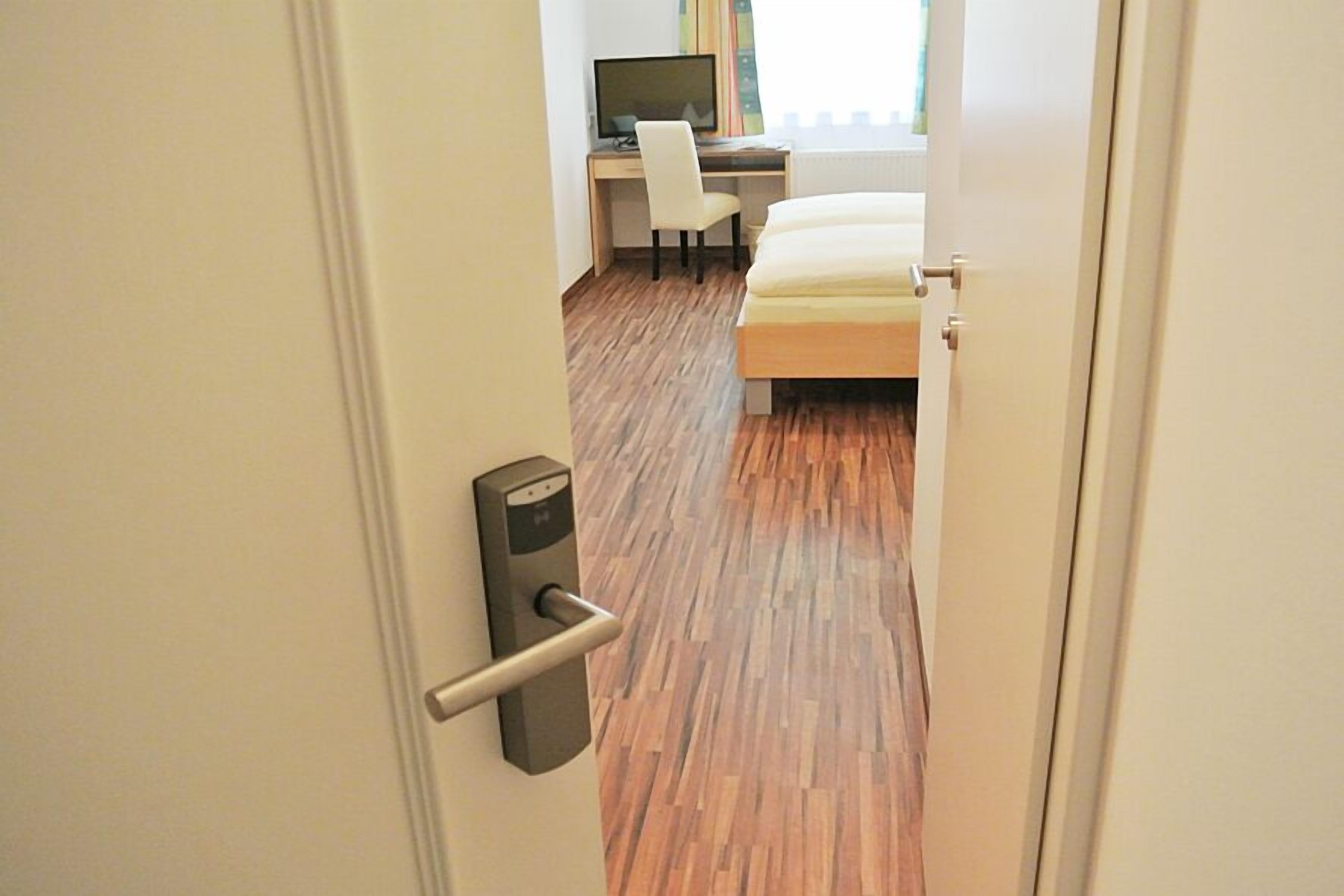 Une chambre d’hôtel avec un plancher en bois, un lit, un bureau avec une chaise et un ordinateur.