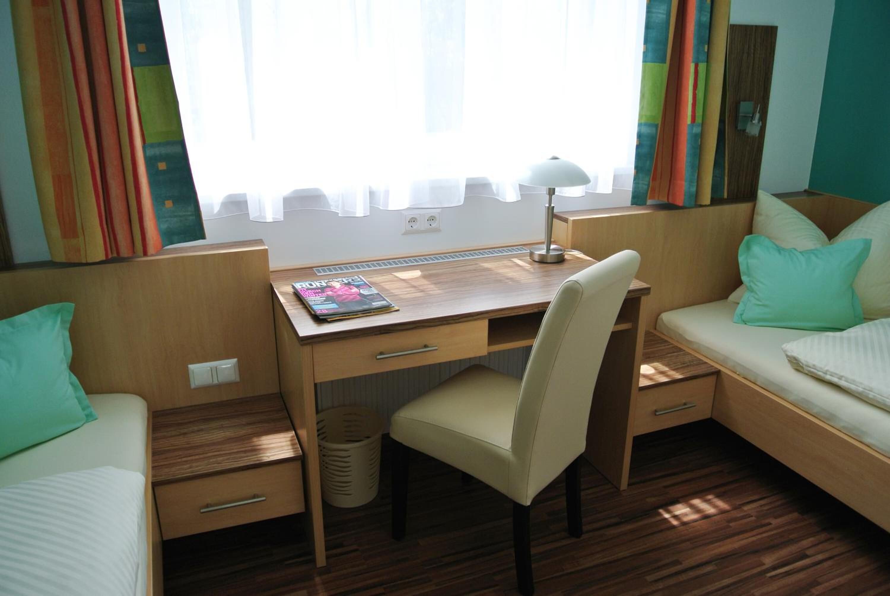 A compact room with a wooden desk, a chair, a bed, and a window with curtains.