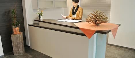 Una recepción con una persona sentada, una planta en maceta y un adorno en el mostrador.