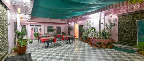 An indoor dining area with tables and chairs, potted plants, and a patterned floor.