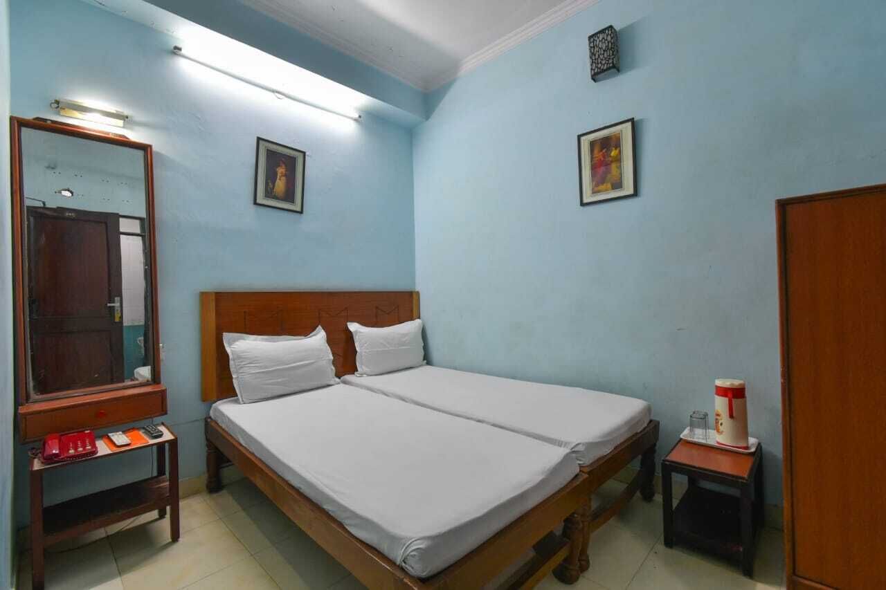 Une chambre avec un lit double, une tête de lit en bois, une table de chevet avec un téléphone rouge, un miroir et une petite table avec une tasse.