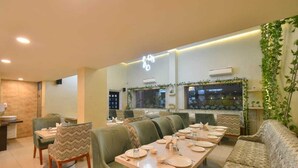 Un restaurante con una mesa larga compartida, asientos acolchados y vistas del paisaje urbano a través de amplias ventanas.