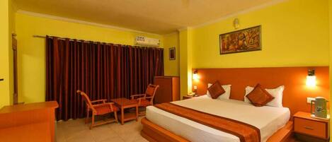 A hotel room with a large bed, a desk, a chair, a ceiling fan, and a painting on the wall.