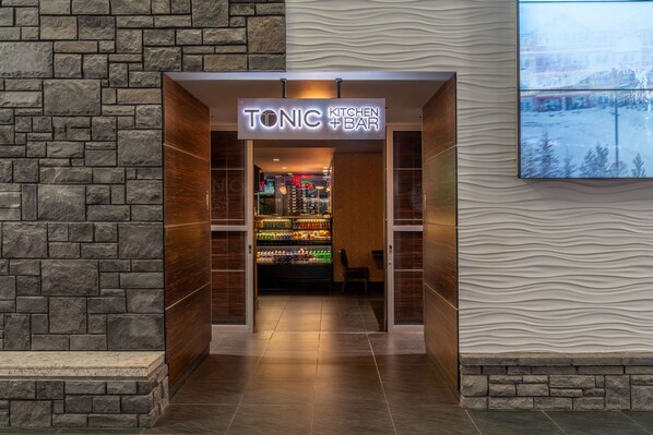 A Tonic Kitchen & Bar entrance with a stone wall backdrop and a modern interior. - Hotel Clique Calgary Airport (Calgary)