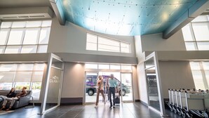 A hotel lobby with a high ceiling, large windows, and a reception area with a van outside. - Hotel Clique Calgary Airport (Calgary)