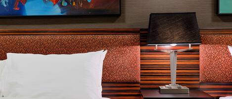 A hotel room with a bed, a nightstand with a lamp, and a colorful abstract painting on the wall.