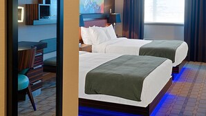 A hotel room with two beds, a desk, a chair, a TV, and a large window with curtains. - Hotel Clique Calgary Airport (Calgary)