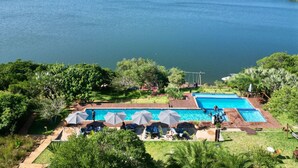 A pool area with multiple swimming pools, surrounded by lush greenery and overlooking a large body of water. - Naara Ecolodge & Spa (Chidenguele)
