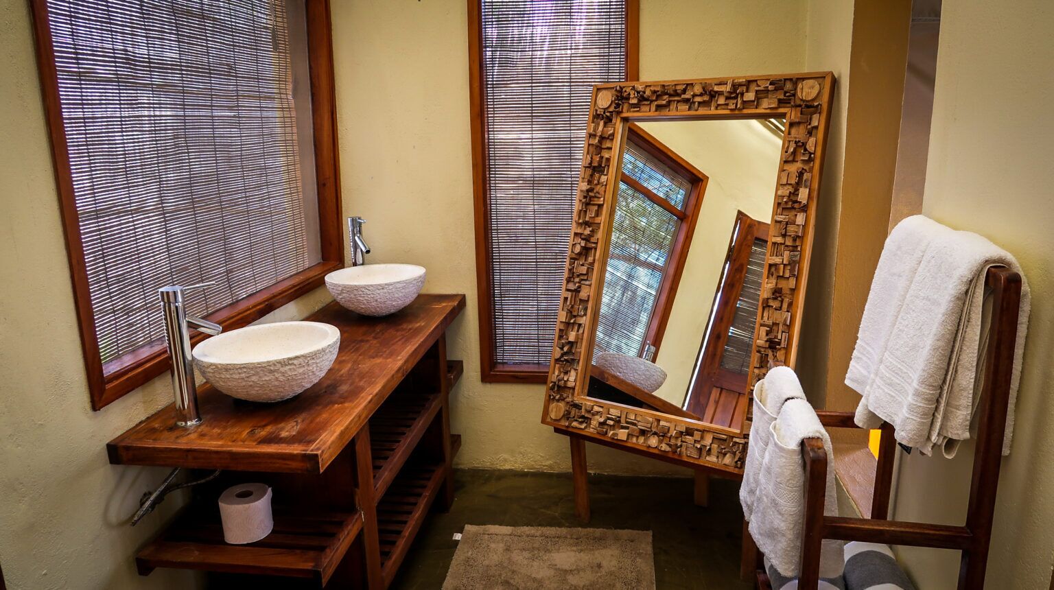 Une salle de bain avec un meuble-lavabo en bois, deux grands lavabos, un miroir et un porte-serviettes.