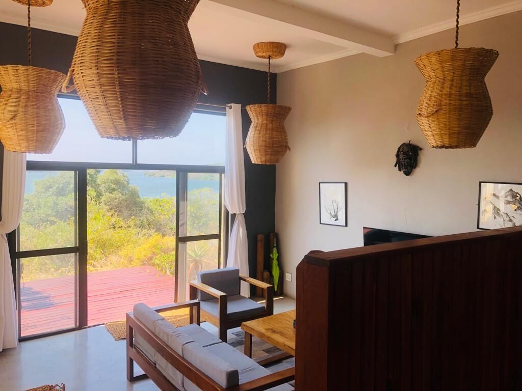 Una habitación con un gran ventanal, lámparas colgantes de mimbre, un banco de madera y un cuadro enmarcado en la pared.