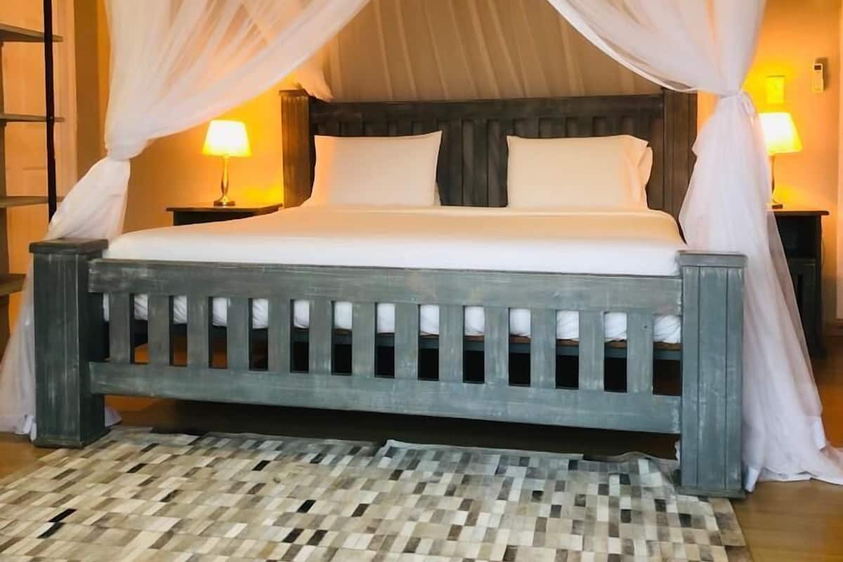 Una cama con estructura de madera y ropa de cama blanca, cubierta por un dosel blanco.