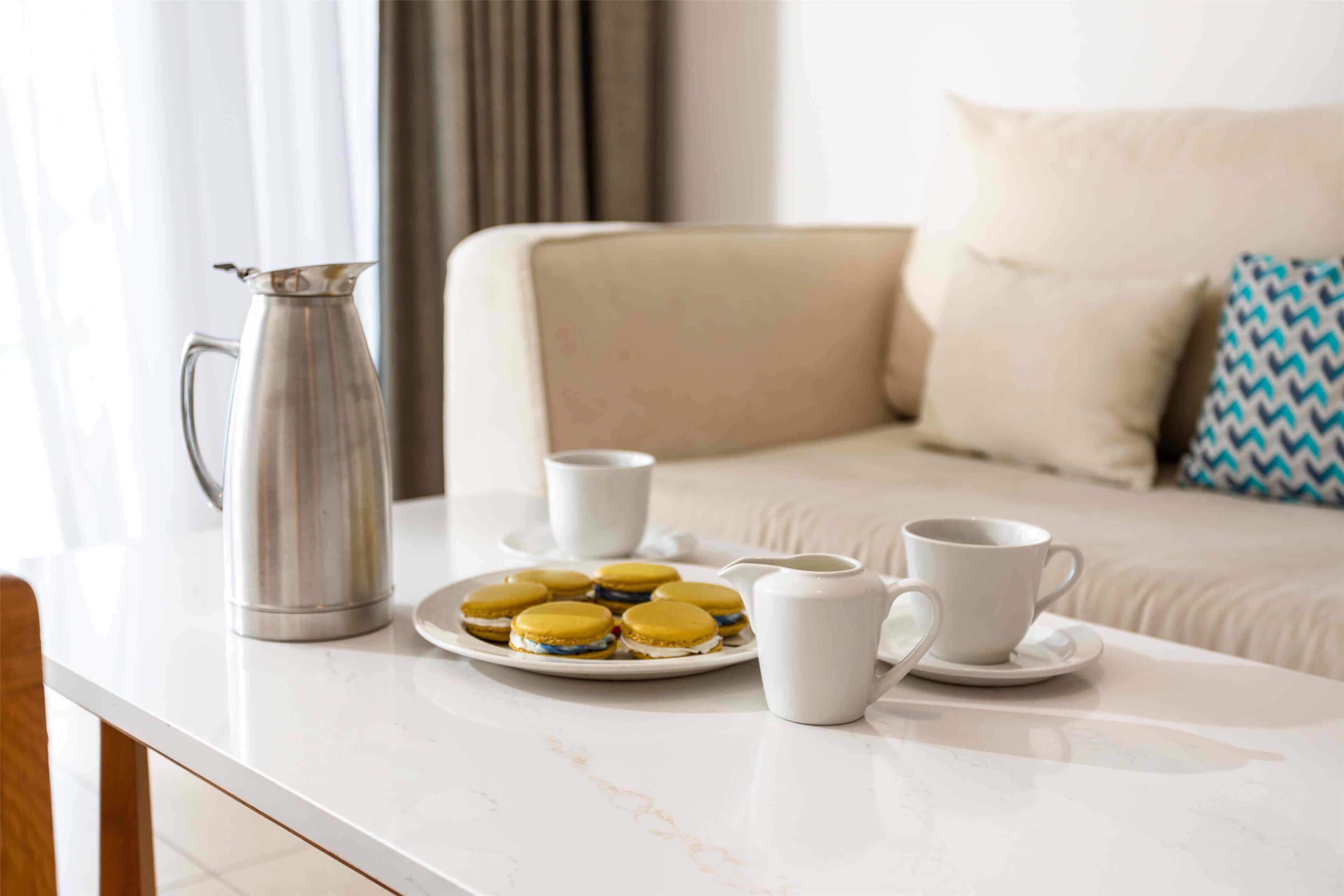 Mesa branca num quarto de hotel com disposição para o café da manhã: pratos com pastéis, um coador de café e duas chávenas.