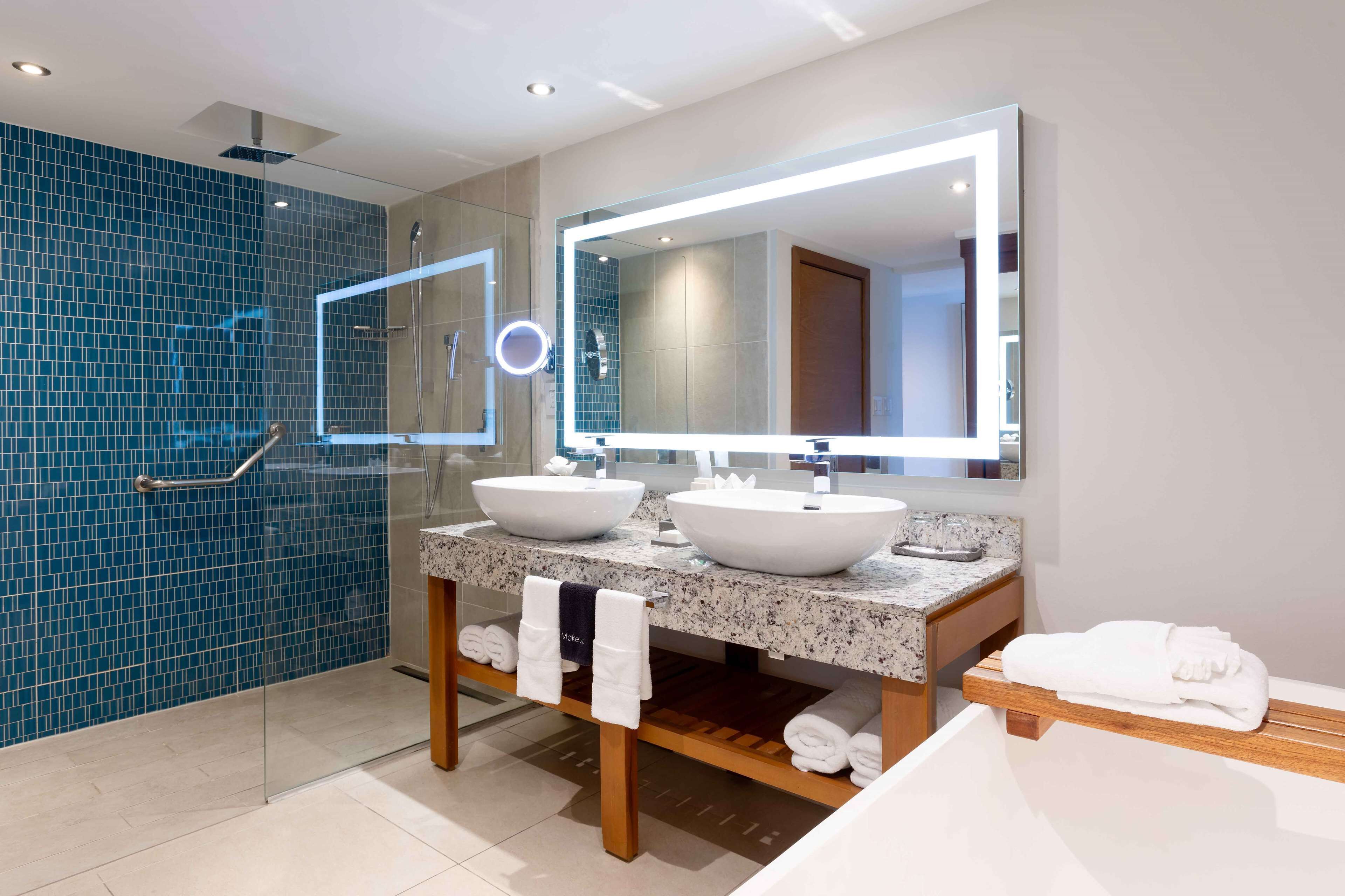 Un baño moderno con dos lavamanos, un espejo grande y una cabina de ducha de vidrio.