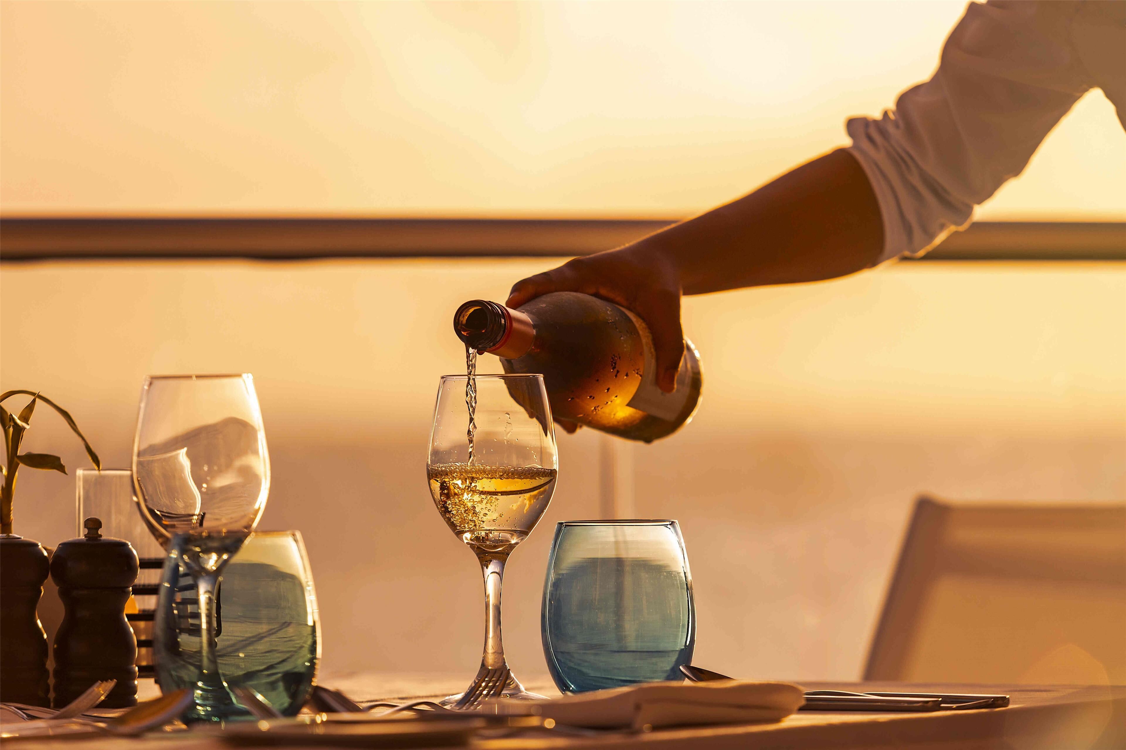 A person pouring a drink into a glass, with other glasses and a salt shaker on a table.