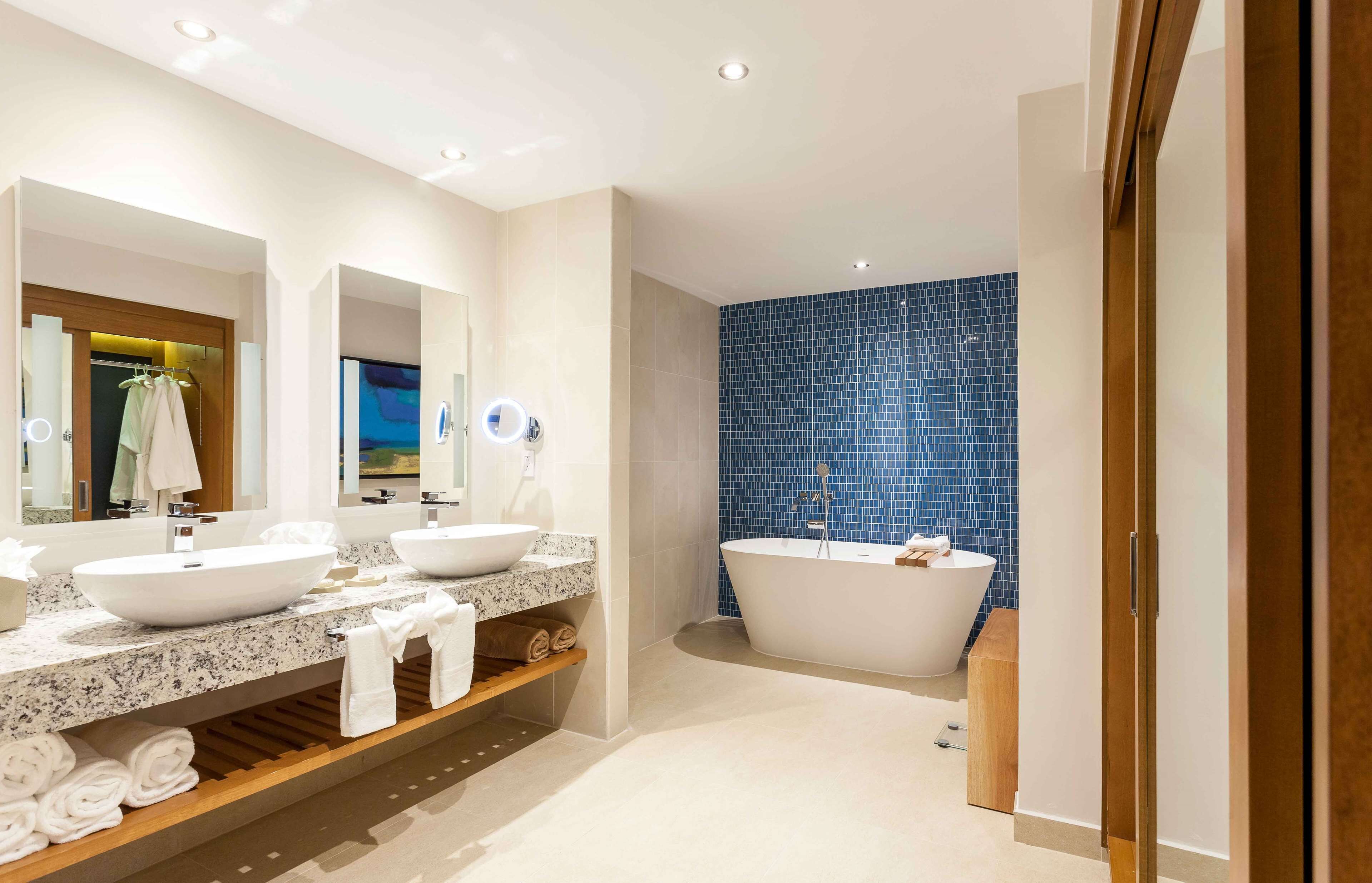 A modern bathroom with two sinks, a freestanding bathtub, and a blue-tiled wall.