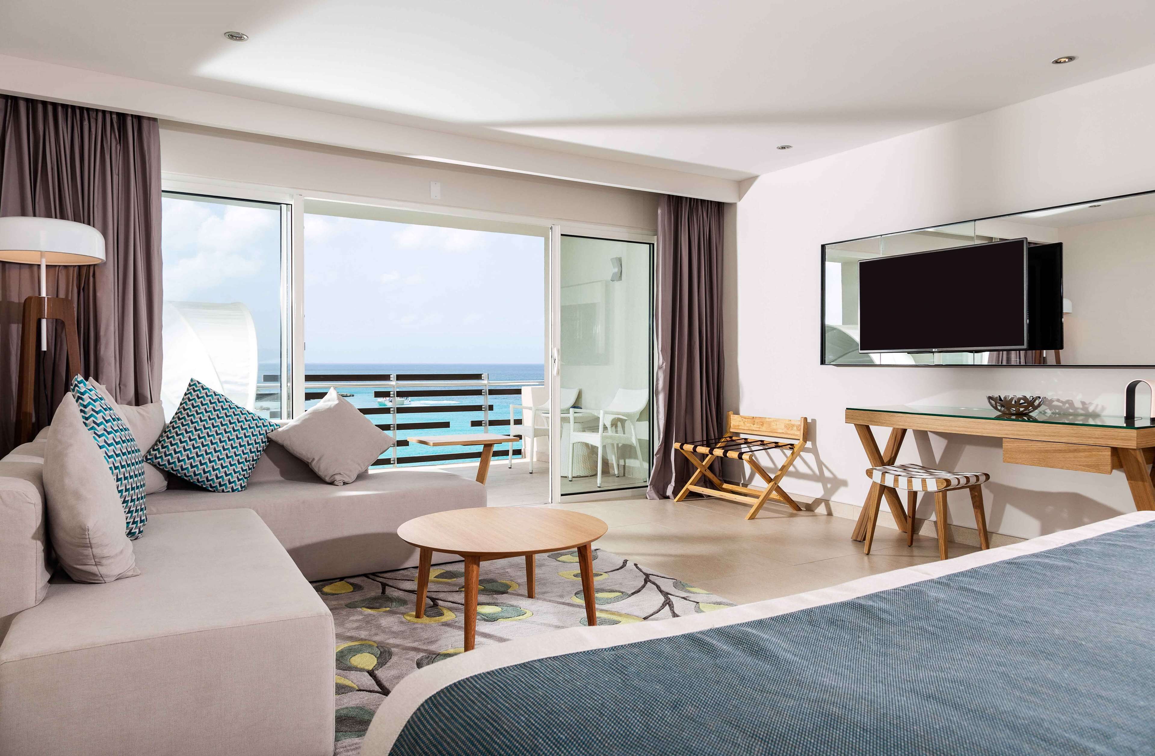 Una habitación de hotel moderna con una cama grande, un sofá, un escritorio y un balcón con vistas al mar.