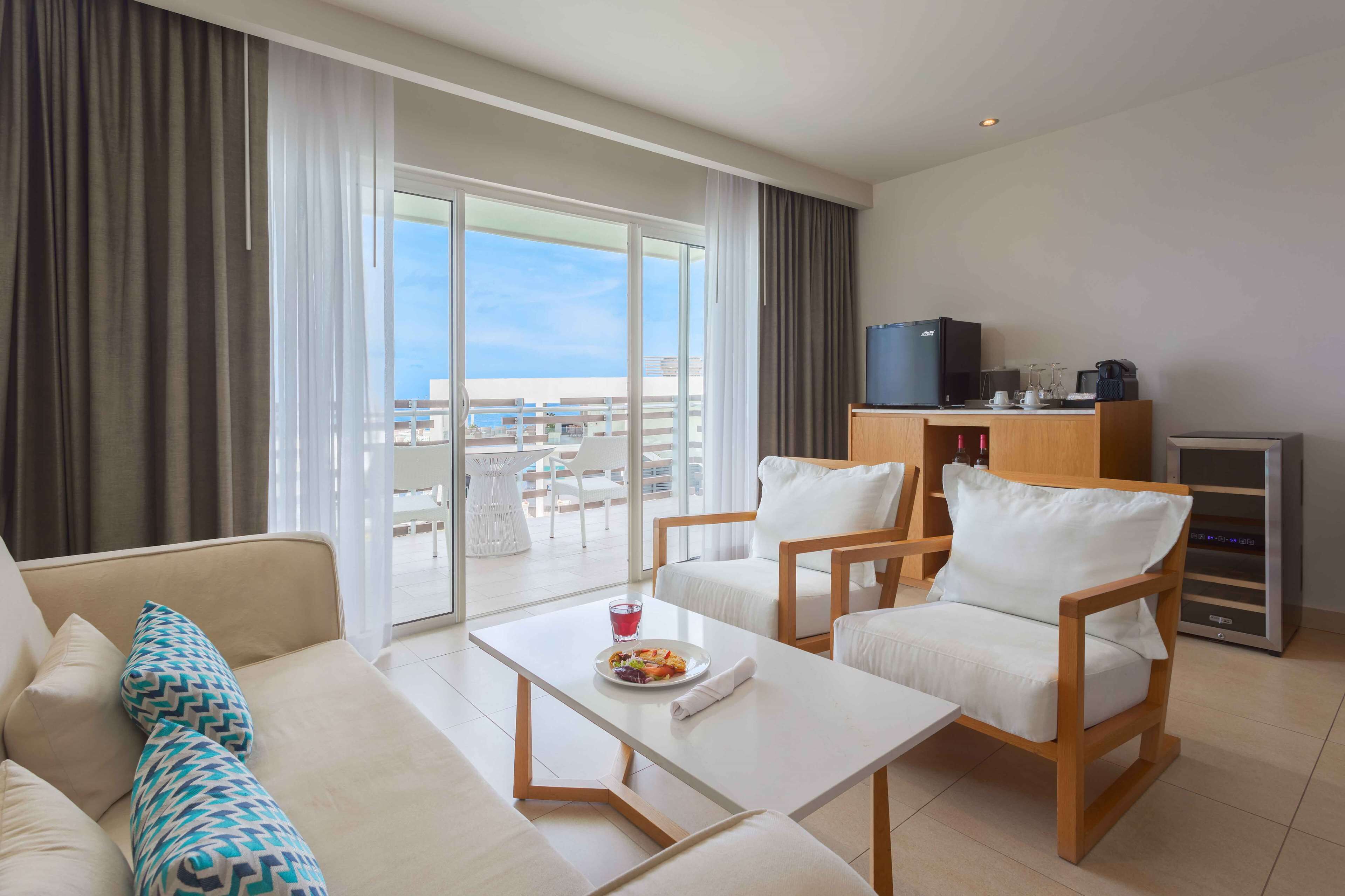 A modern hotel room with a balcony, a dining area, and a TV.
