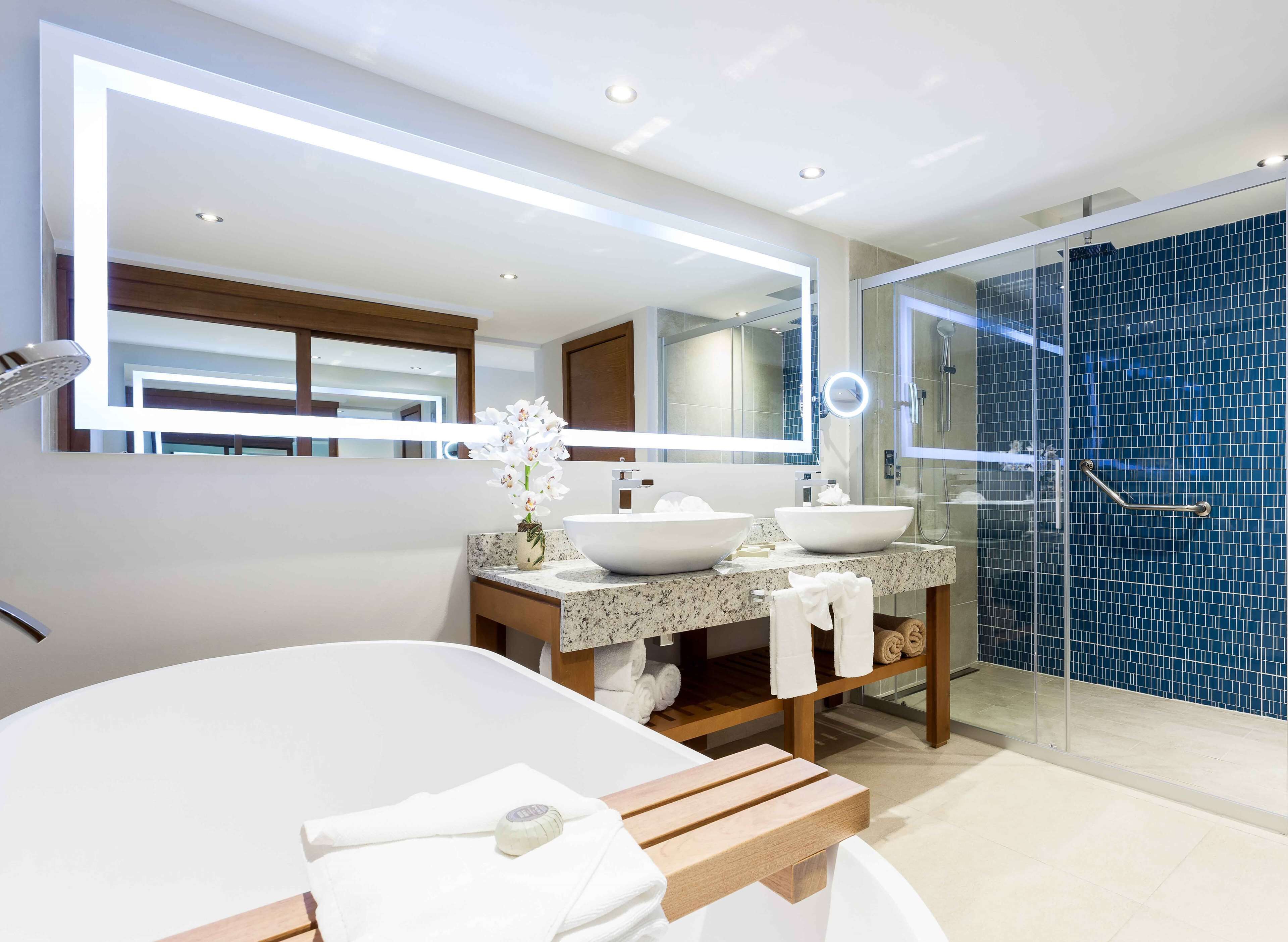 Un baño moderno con una bañera grande, dos lavamanos, ducha con mampara de vidrio y tocador con espejo.