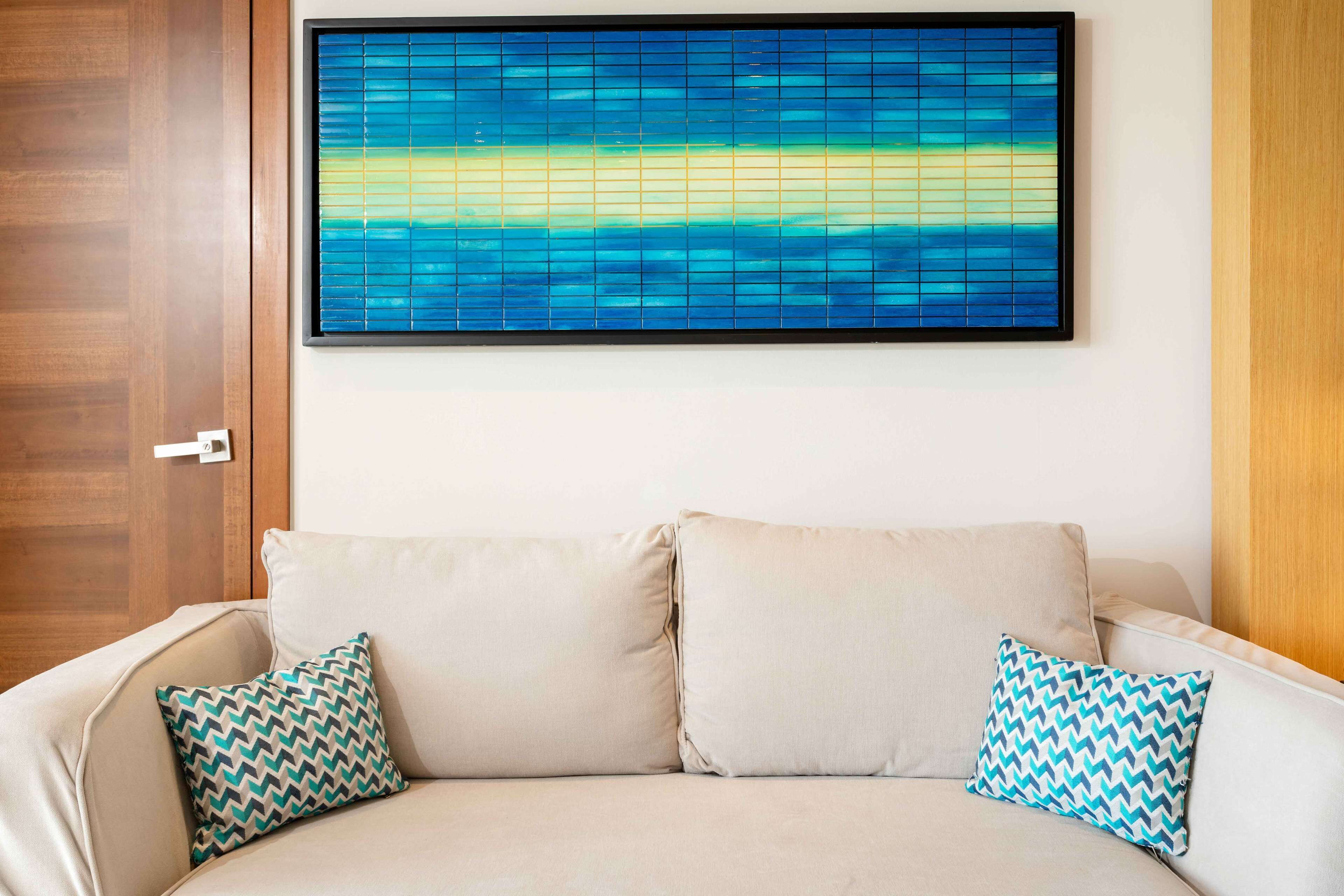 A beige sofa with two patterned pillows, a large abstract painting, and a wooden door.