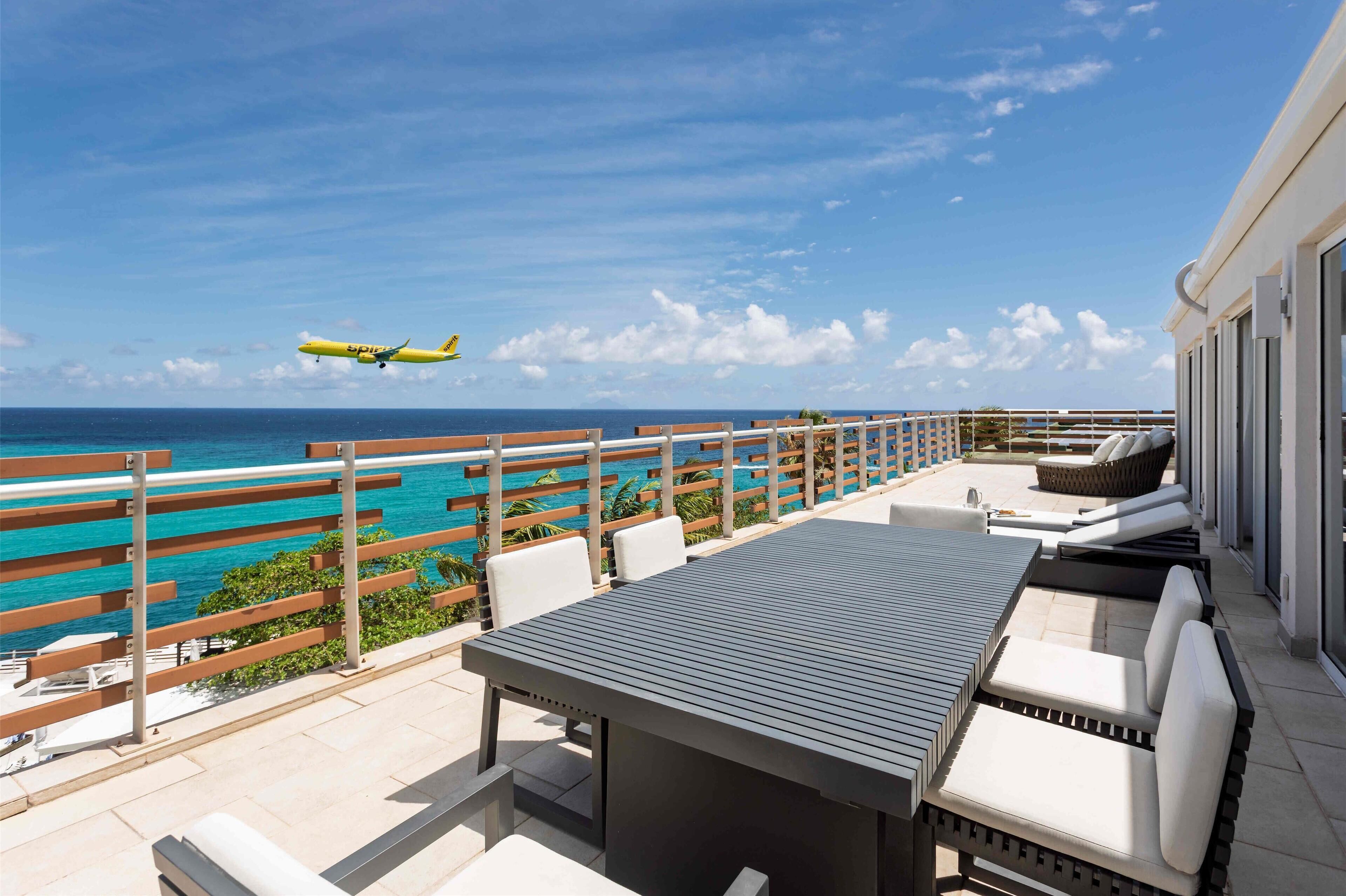 Une terrasse extérieure offrant une vue sur l’océan et sur un avion dans le ciel.