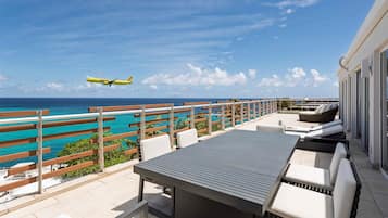 An outdoor patio with a view of the ocean and a plane in the sky.