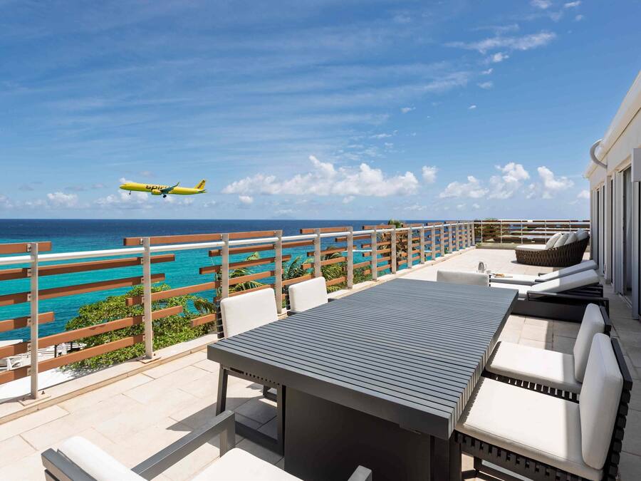 An outdoor patio with a view of the ocean and a plane in the sky.