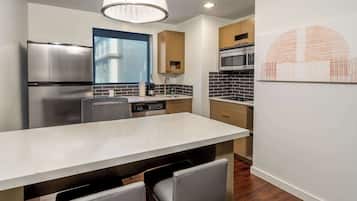 Una cocina moderna con un refrigerador de acero inoxidable, lavavajillas integrado, una isla grande con asientos y una lámpara colgante.