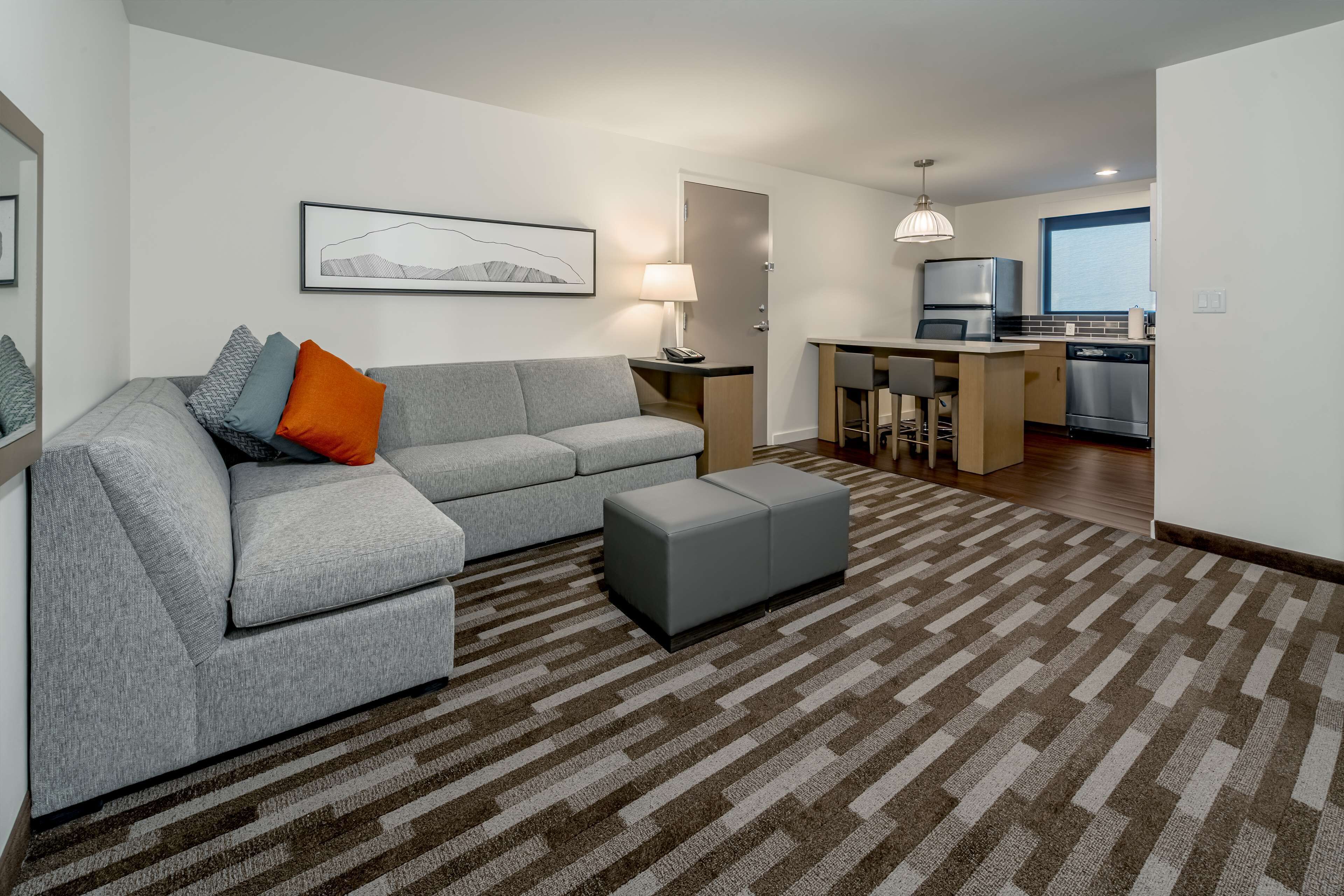 Un salon moderne avec un canapé gris, un tapis à motifs et un coin cuisine comprenant une table à manger et des chaises.
