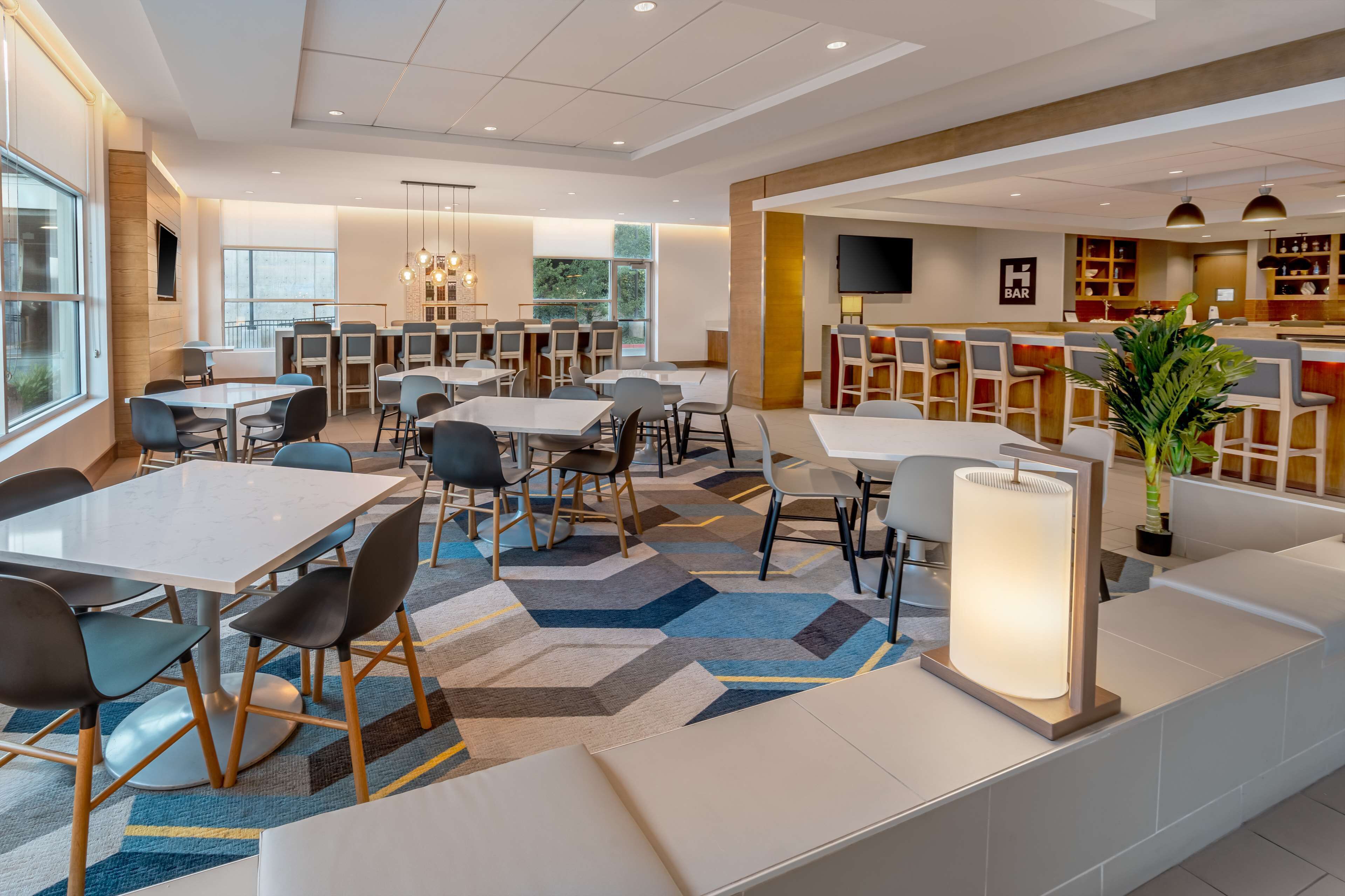 Un espace repas moderne avec des tables et des chaises, un bar et une grande plante.