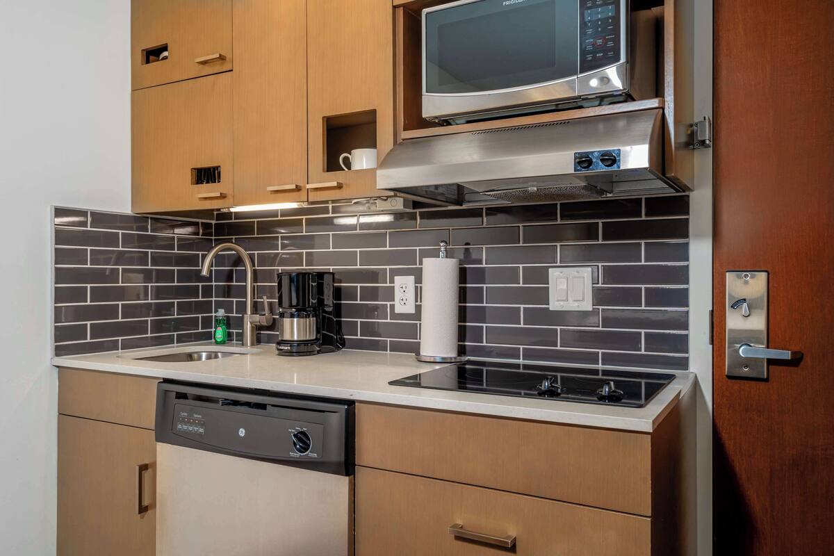 A modern kitchen with wooden cabinets, a stainless steel microwave, a coffee maker, and a dishwasher.