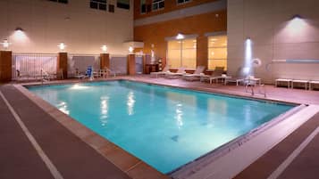 An indoor swimming pool with lounge chairs and a changing room area.