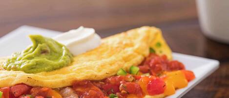 Prato de café da manhã com omelete enrolada, tomates em cubos e abacate sobre um prato branco.