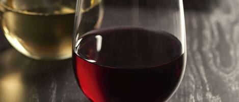 Two glasses of wine on a wooden table with a bottle and some food items in the background.