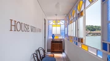 A hallway with a view of the sea, a wooden chest of drawers, and a blue chair.