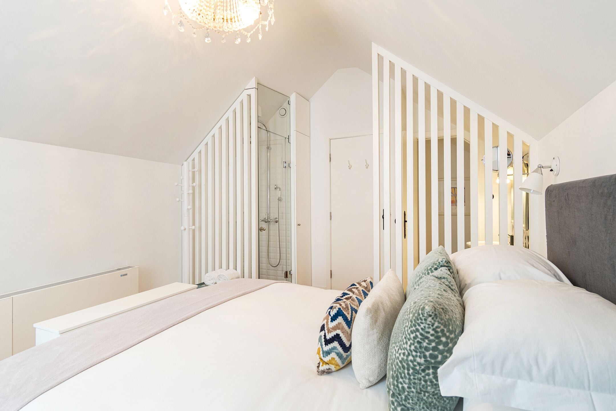 A bedroom with a bed, pillows, a nightstand, a dresser, a mirror, and a shower.