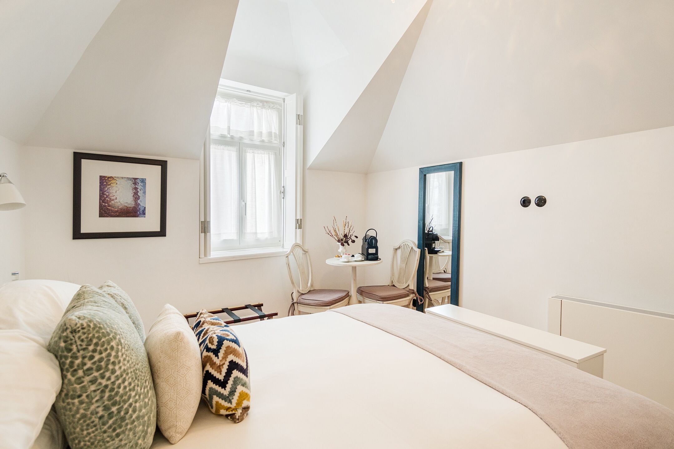 A bedroom with a bed, a desk, two chairs, a window, and a framed picture on the wall.