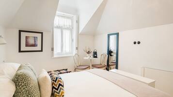 A bedroom with a bed, a desk, two chairs, a window, and a framed picture on the wall.