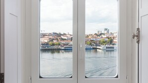 Vista a través de una puerta blanca con dos ventanas, mostrando un paisaje urbano con edificios, un río y barcos.