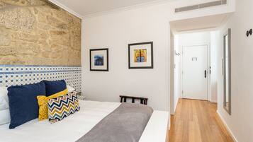 Un dormitorio con pared de piedra, una cama con almohadas azules y amarillas, una manta gris y dos cuadros enmarcados en la pared.