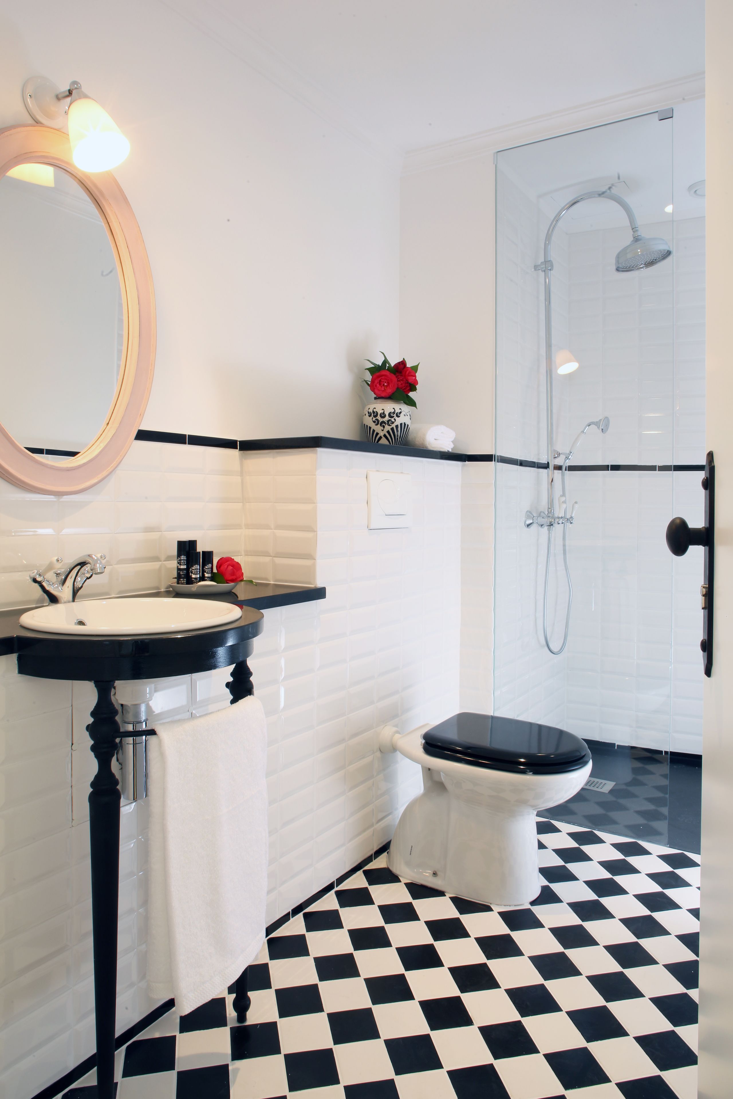 Une salle de bain avec un carrelage noir et blanc, un lavabo blanc avec un plan de toilette noir, des toilettes blanches et une douche séparée par une paroi en verre.