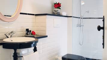 Une salle de bain avec un carrelage noir et blanc, un lavabo blanc avec un plan de toilette noir, des toilettes blanches et une douche séparée par une paroi en verre.