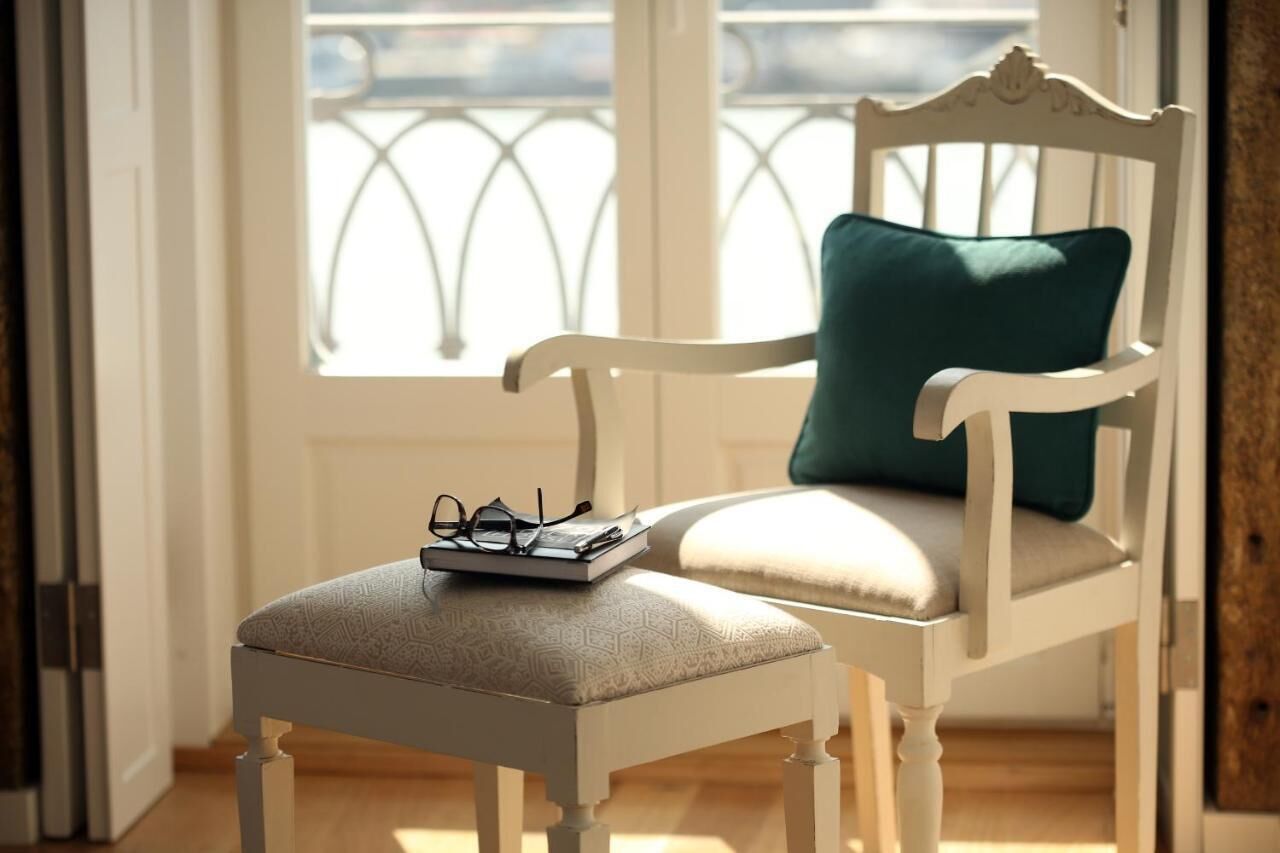 A white chair with a cushion and a green pillow, a pair of glasses, and a book on the seat.