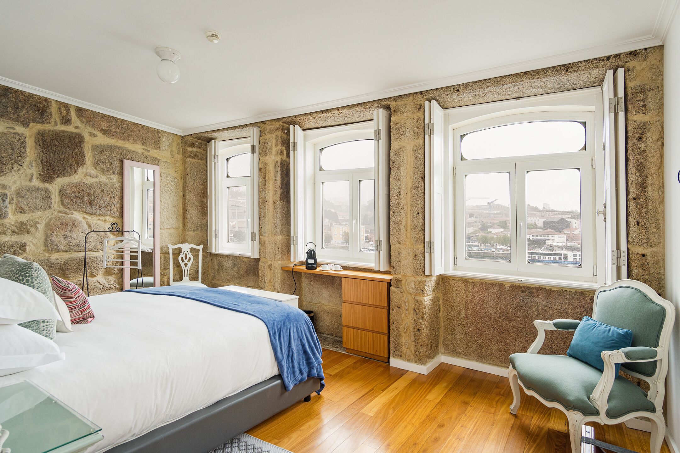 A bedroom with a stone wall, wooden desk, and a view of the city.