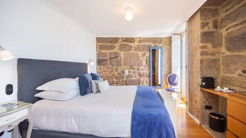 A bedroom with a large bed, a stone wall, a wooden dresser, and a desk with a lamp.