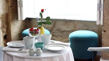 A table set with white plates, bowls, and cups, a vase with a rose, and a bowl of strawberries.