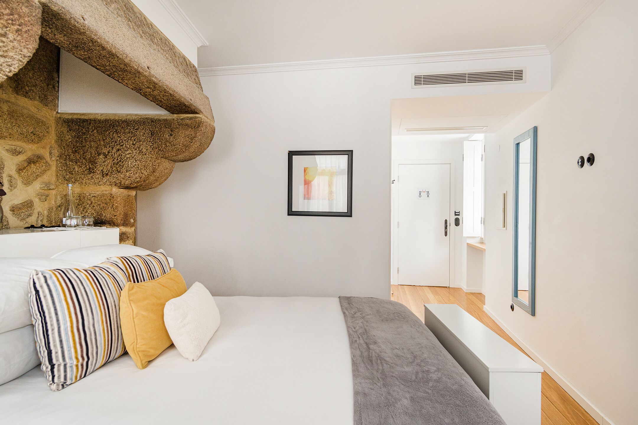 Um quarto com lareira de pedra, cama com almofadas listradas e de cor lisa, um quadro emoldurado na parede e um espelho na parede.