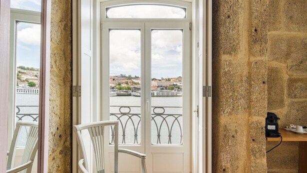 Una habitación con vista a un río y edificios, una puerta blanca, una silla y una pequeña mesa con objetos encima.